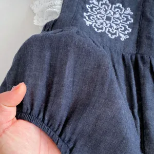 Detalle de mameluco para bebé con tela oscura suave, elegante bordado blanco y encaje fino.