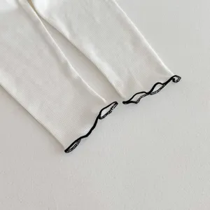 Close-up detail of white ribbed baby leggings with black lettuce edge trim on the cuffs.