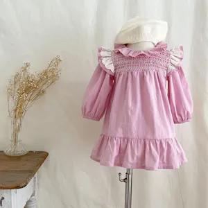 Abito rosa a maniche lunghe per bambina con corpetto arricciato e dettagli in pizzo.
