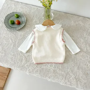 Detailed view of baby knitted vest with cute strawberry embroidery, cozy table flat lay scene.