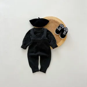 Detail shot of infant black knitted sweater and overalls set with beret and shoes on tray.
