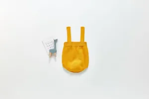 Vue détaillée d'une barboteuse pour bébé en tricot jaune uni, modèle bretelles.