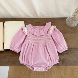 Dettaglio tutina maniche lunghe bimba rosa, dolce collo volant e petto ricamato a nido d'ape.