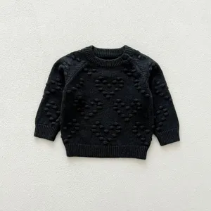 Close-up of black infant knit sweater with textured heart patterns and shoulder snap buttons.