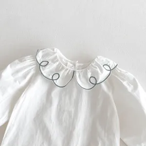 Detailed close-up view of infant white long-sleeve top with green embroidered collar.