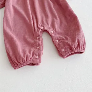 Détail de barboteuse bébé en velours côtelé, combinaison rose mûre à manches longues boutons.