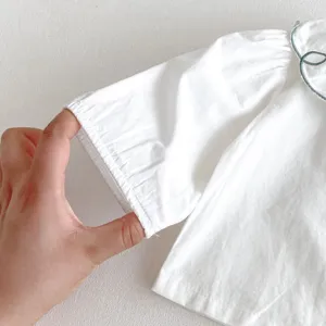 White baby shirt sleeve detail, soft cotton fabric, fine stitching for infant daily wear.