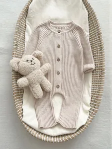 Detailansicht eines kuscheligen beigen Baby-Stramplers aus Strick mit Knöpfen und Bär.