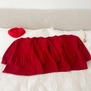 Detailed view of cozy red knit toddler dresses arranged neatly on white bedding setup.
