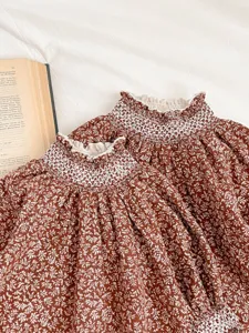 Detailed view of cute baby girl floral print dress with smocked high neck and lace trim.