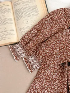 Detailed close-up shot of brown floral baby dress sleeve featuring elegant white lace cuff trim.