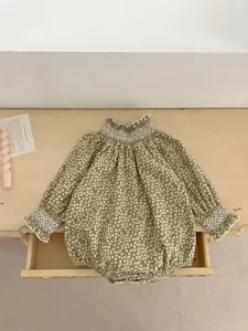 Infant long sleeve floral romper detail, showing smocked collar and cuffs on wood background.
