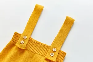 Gros plan sur les détails des bretelles de barboteuse bébé en tricot jaune, doux.