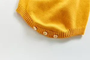 Détail de barboteuse en tricot pour bébé, matière jaune douce avec de jolies boutons en bois.