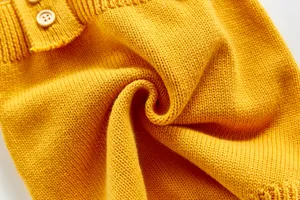 Gros plan sur le tissu tricoté jaune pour bébé, montrant une texture douce et des boutons.