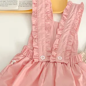 Dettaglio vestito neonata rosa, spalline con volant carine e bottoni a fiore, tessuto morbido.