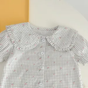 Dettaglio camicia manica corta a quadri con stampa floreale e colletto con volants.