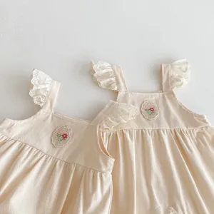 Dettaglio abito con bretelle per bambina, volant in pizzo e ricamo floreale.