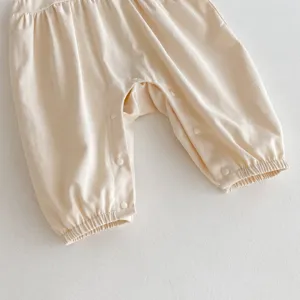 Dettaglio pantaloni tutina neonato monocolore, tessuto beige chiaro, bottoni a pressione.