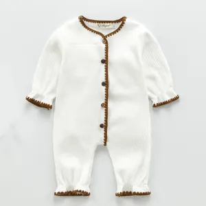 Detailansicht des weißen Baby-Stramplers mit brauner Häkelborte und Holzknöpfen.
