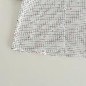 Dettaglio camicia per neonati con grazioso motivo a quadri e ciliegie, tessuto e bottoni.