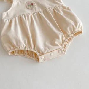 Dettaglio tutina per neonato, grazioso body beige in cotone con toppa ricamata di fiori.
