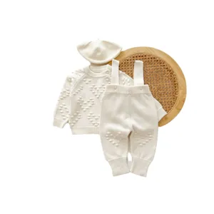 Cute baby knitwear set with beret sweater and suspender pants in cozy cream color.