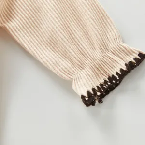 Nahaufnahme des feinen Baby Strampler Ärmels in Beigefarben mit schickem braunem Bündchen.