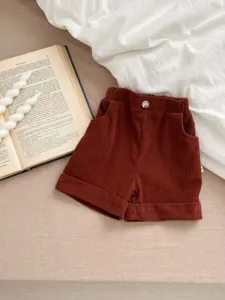 Detailed view of kids brown corduroy shorts, featuring front button, pockets and rolled cuffs.