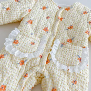 Detailed view of baby quilted jumpsuit with cute orange floral print and white lace pockets.