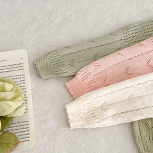 Gros plan détaillé de manches de cardigan en tricot ajouré pour bébé aux teintes douces.