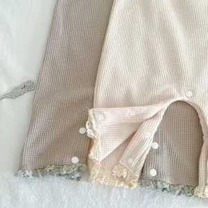 Waffelstrick Baby Jumpsuit Detail, weicher Stoff, Spitzenborte und praktische Druckknöpfe.