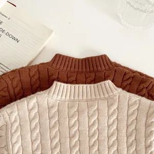 Nahaufnahme Detail des Baby Zopfmuster Pullovers in kuscheligem Beige und Braun, flachgelegt.