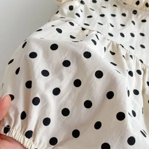 Infant baby girl cotton romper detail, cute black polka dot pattern on soft beige fabric.