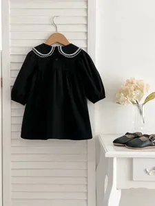 Vestito nero a maniche lunghe per neonata con colletto ricamato bianco. Dettaglio.