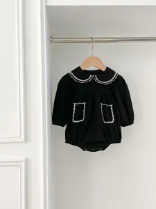 Dettaglio tutina nera per neonata, colletto con risvolto ricamato bianco e doppie tasche frontali.
