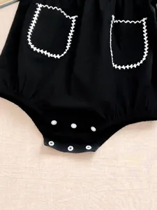 Dettaglio di tutina neonato nera con tasche ricamate in bianco e bottoni a pressione.