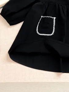 Primo piano del vestito nero a maniche lunghe per neonata con tasca ricamata bianca.