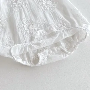 Close-up detail of white baby romper with delicate floral embroidery and snap buttons.