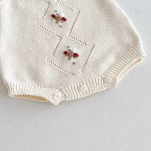 Close-up detail of knitted baby romper, cream white color with cute embroidery and texture.