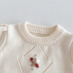 Infant beige knit sweater detail featuring delicate embroidery and elegant diamond pattern.