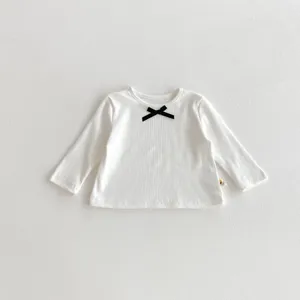 Close-up details of white ribbed toddler long sleeve shirt featuring a cute black bow accent.