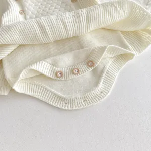 Detailed view of baby girl white knitted romper with cute buttons and ribbed cuffs for cozy wear.