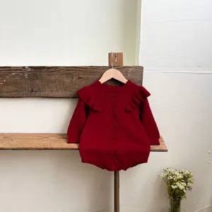 Vista dettagliata della tutina neonato in maglia rossa con volant e motivo a rombi.