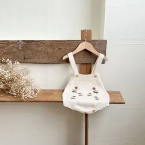 Primo piano della tutina in maglia per neonato con delicato ricamo floreale e bottoni in legno.
