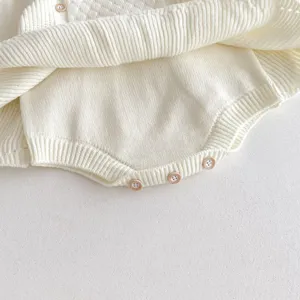 Close-up detail of infant knitted baby romper, soft knit texture and wood buttons.