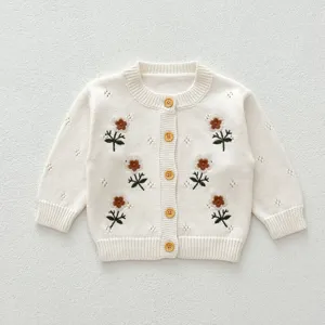 Dettaglio del cardigan in maglia per neonati con ricamo floreale e bottoni in legno beige.