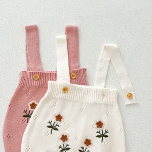 Vista dettagliata di tutine in maglia per neonati con ricamo floreale e bottoni in legno raffinati.