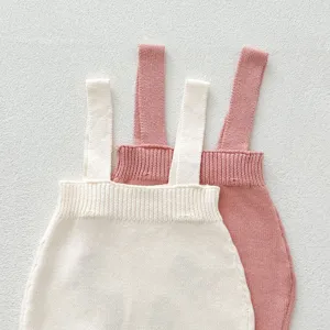 Primo piano di tutine con bretelle in maglia per neonati color avorio e rosa, trama fine.