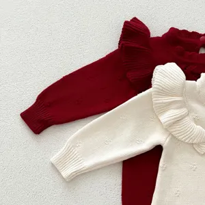 Dettaglio in primo piano della tutina in maglia per neonato, con volant delicati e morbida texture.